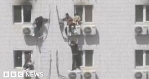 People cling to aircon units on side of burning hospital
